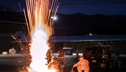 Pyrotechnic explosion with orange sparks shooting upward during nighttime fire training exercise.