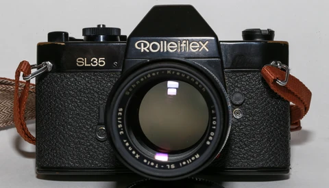 Rollei SL35 film camera with Carl Zeiss lens and brown leather neck straps on gray background.