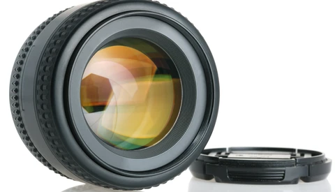 Camera lens with amber-tinted glass elements and detached rear cap on white surface.