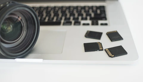 Camera lens and memory cards arranged on a laptop keyboard.