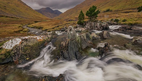 Mountain stream with smooth, flowing water cascading over layered rock formations in a misty valley.