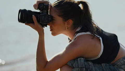 Female photographer holding a professional film camera to her eye while composing a shot outdoors.