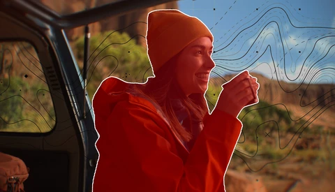 Person in red jacket and beanie leaning out of vehicle window against desert landscape.