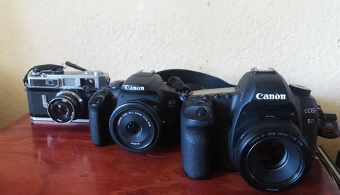 Three Canon cameras arranged in chronological order on a wooden surface, ranging from vintage rangefinder to modern DSLR.