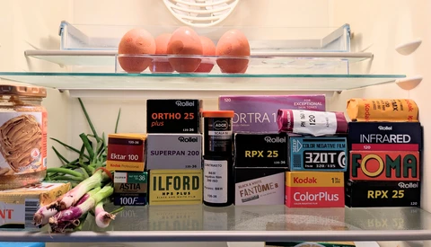 Refrigerator shelf displaying vintage film stock boxes and fresh produce including apples and vegetables.