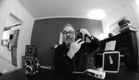 Photographer holding a rangefinder camera in a black and white self-portrait taken with a wide-angle lens.
