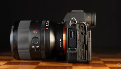 Sony mirrorless camera with attached telephoto lens on wooden surface against dark background.