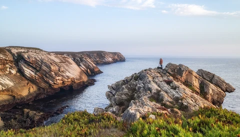 Rugged coastal cliffs with golden-hour sunlight illuminating rocky outcrops and a solitary sea stack.