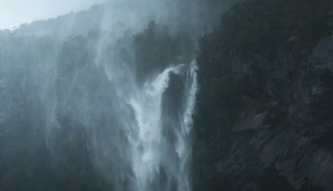 Misty waterfall cascading down a forested mountainside shrouded in fog.