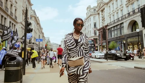 Woman in zebra-striped outfit walking on busy urban street lined with classical buildings.