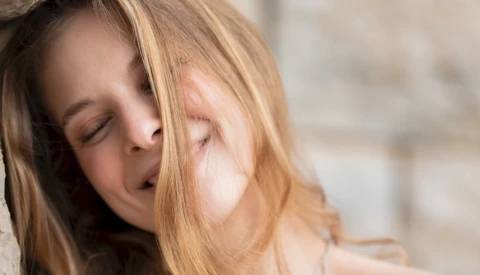 Woman with reddish-brown hair tilting her head with eyes closed in soft natural light.