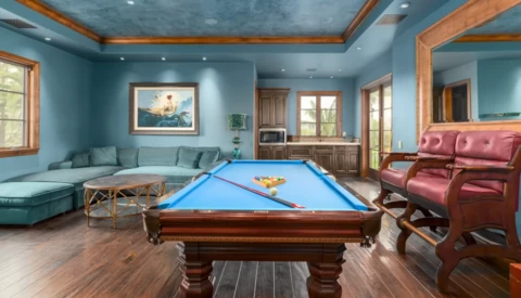 Billiards table with blue felt in a turquoise recreation room with wood ceiling beams.