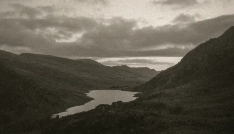 Mountain valley landscape with winding river and dramatic cloudy sky in monochrome.