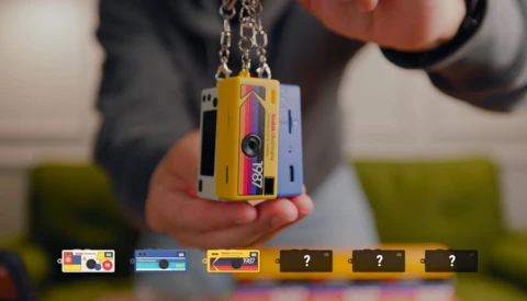 Person holding a yellow and pink instant camera pendant on a chain.