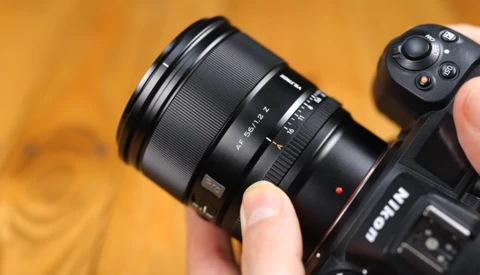 Close-up of a camera lens being held and adjusted by hand against a warm golden background.