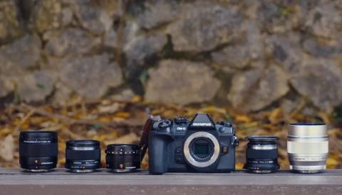 Olympus OM camera body with five interchangeable lenses arranged in a product lineup.
