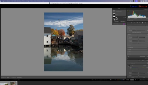 Waterfront buildings with autumn trees reflected in still water beneath blue sky.