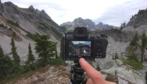 Camera mounted on tripod displaying mountain valley landscape on its rear screen.