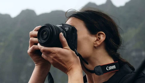 Photographer with Canon camera capturing landscape with dramatic mountain peaks in background.