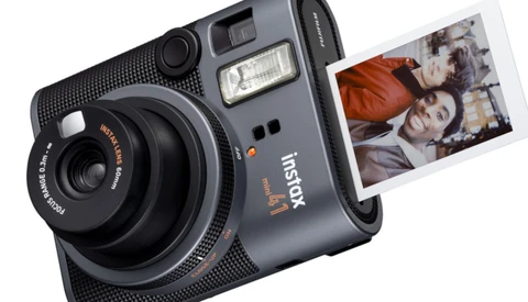 Instax hybrid instant camera with built-in flash and control dial, ejecting a printed photograph showing two people.