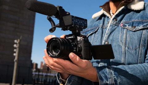Videographer holding a cinema camera with an external monitor and microphone mounted on an urban rooftop.