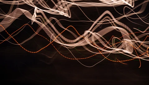 Light painting photograph with flowing curves of orange and white light trails against black background.