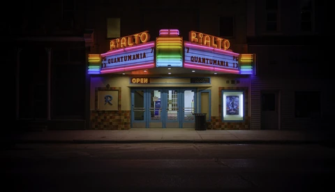 Vintage movie theater facade illuminated by neon signs at night, with colorful rainbow-spectrum lettering and marquee.
