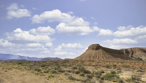 Distinctive cone-shaped butte rising from arid desert landscape under partly cloudy sky.