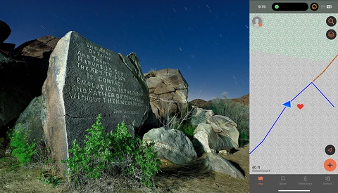 Memorial stone with engraved text positioned among large boulders under clear blue sky.