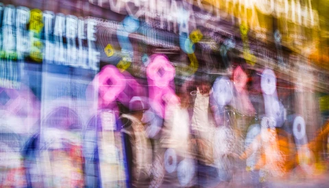 Blurred neon signs and pedestrians on an urban street at night, with magenta and blue glowing lights.