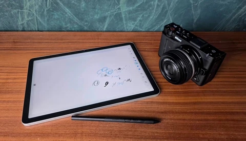 Digital tablet with stylus and vintage film camera on wooden desk.