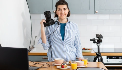 Woman holding a telephoto lens in a home studio setup with a tripod-mounted camera and ring light.