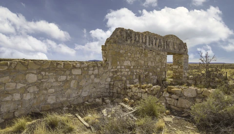 Ruined stone structure with rectangular opening in arid landscape under cloudy sky.