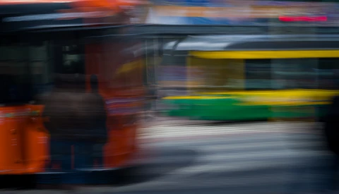 Multiple buses in motion blur during evening hours with warm and cool lighting.