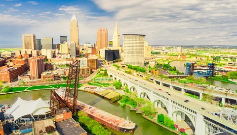 Aerial view of a Midwest city skyline with downtown towers reflected in a river bend.