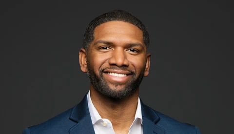 Professional headshot of a man wearing a dark blue blazer and white dress shirt against a dark gray background.