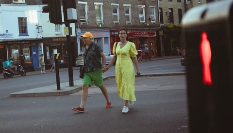 Two joggers crossing a city street at a red traffic light in bright daylight.