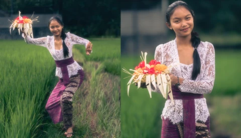 Woman in lace cardigan and burgundy skirt holding glowing red flower arrangement in rice field.