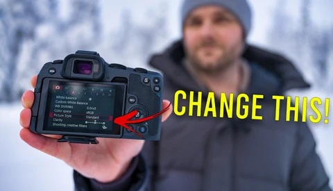 Photographer holding mirrorless camera with LCD screen displaying menu settings in snowy outdoor environment.