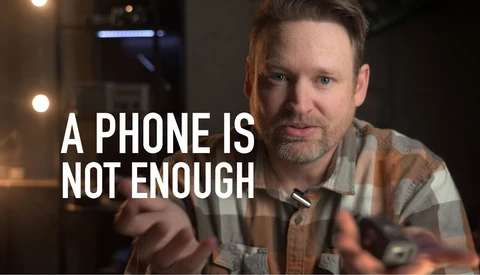 Man in plaid shirt gesturing while speaking, with text overlay reading "A PHONE IS NOT ENOUGH."