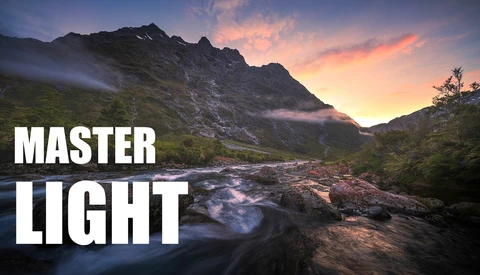 Mountain landscape at sunset with a flowing river in the foreground and dramatic sky.