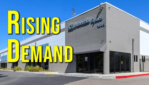 Modern industrial building with large storefront and yellow text overlay reading 'Rising Demand' against clear blue sky.