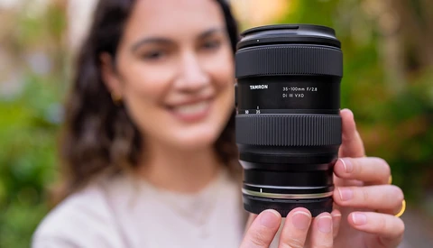 Person holding a Tamron 24-105mm f/2.8 telephoto lens toward the camera in an outdoor setting.