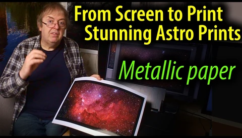 Man holding a metallically-printed astrophotography image showing a vibrant red and pink nebula with stars.