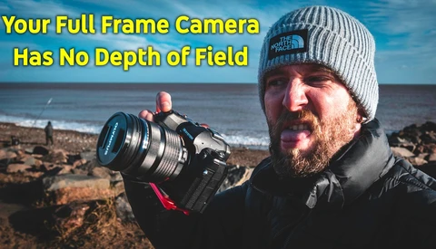 Photographer holding a full-frame camera with telephoto lens on a rocky beach at sunset.