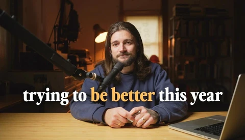 Podcaster speaking into a microphone at a desk with a laptop, shot in warm studio lighting.