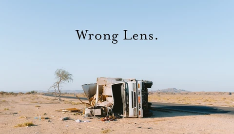 Overturned vehicle lying on its side in an arid desert landscape with sparse vegetation.