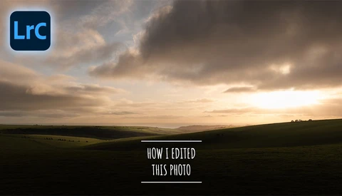 Dramatic landscape at sunset with rolling hills silhouetted against a moody sky with golden and gray clouds.