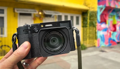 Black rangefinder camera with textured grip held in hand against urban backdrop.