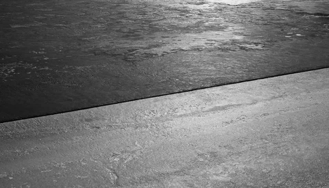 Dark water meeting a concrete edge in sharp contrast, minimal geometric composition.